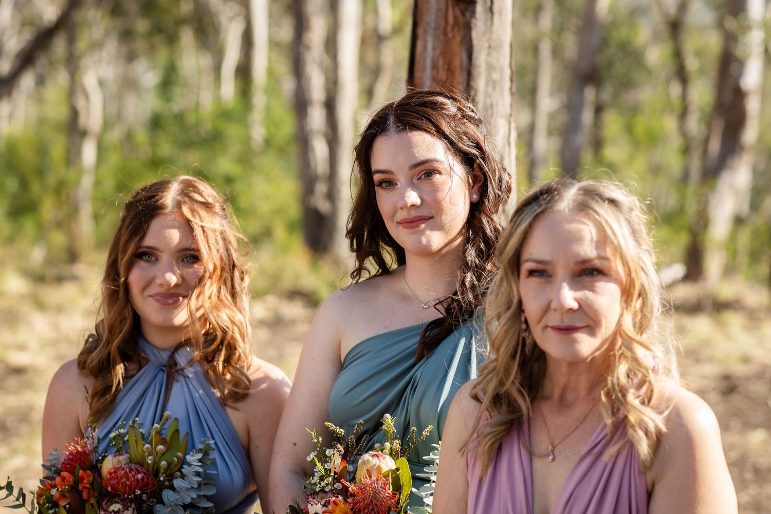 Row of bridesmaids in varying shades of pink and blue dresses holding autumn bouquets.