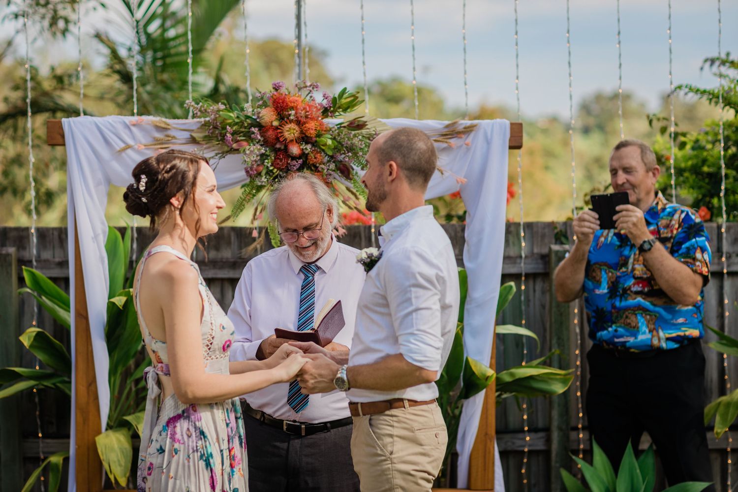 Wedding ceremony takes place under hanging string lights in a tropical garden setting.Gold Coast beach wedding photography