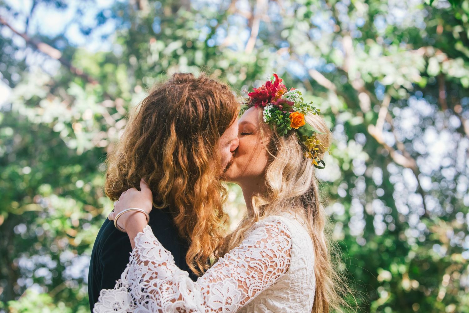 Romantic outdoor wedding moment with couple kissing surrounded by greenery and floral decorations.