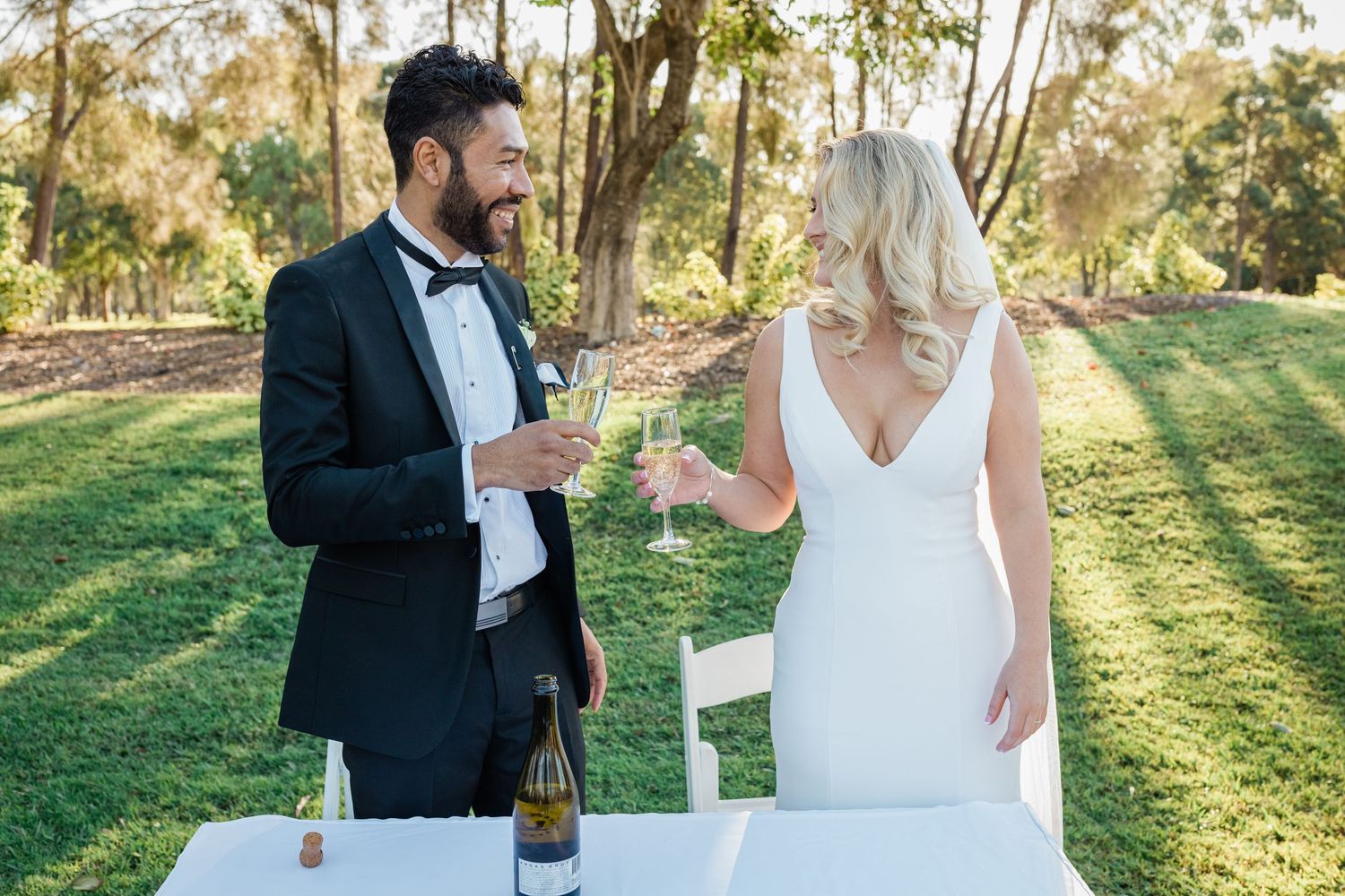 Wedding couple and guests celebrate with champagne toasts in a sunlit outdoor garden setting.