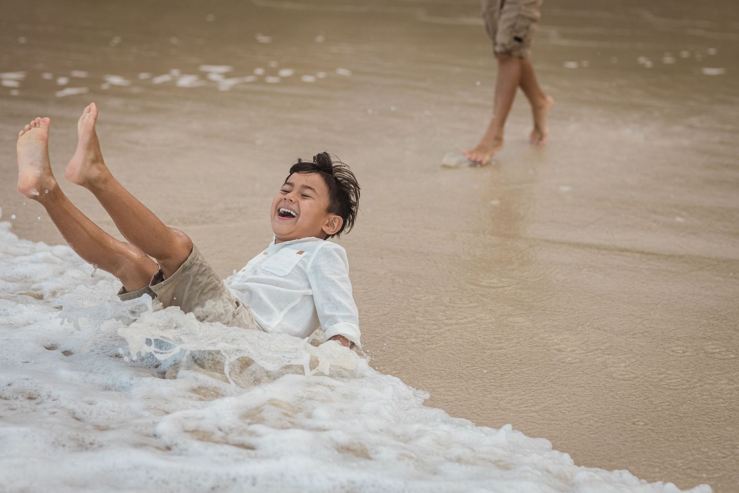 Joyful moments of splashing and playing in beach waves at sunset.Gold Coast candid family photographer.