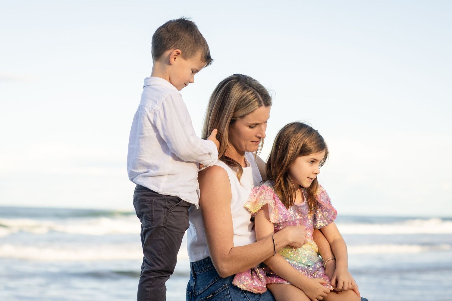 Casual beach family portrait with ocean waves and natural lighting in the background.