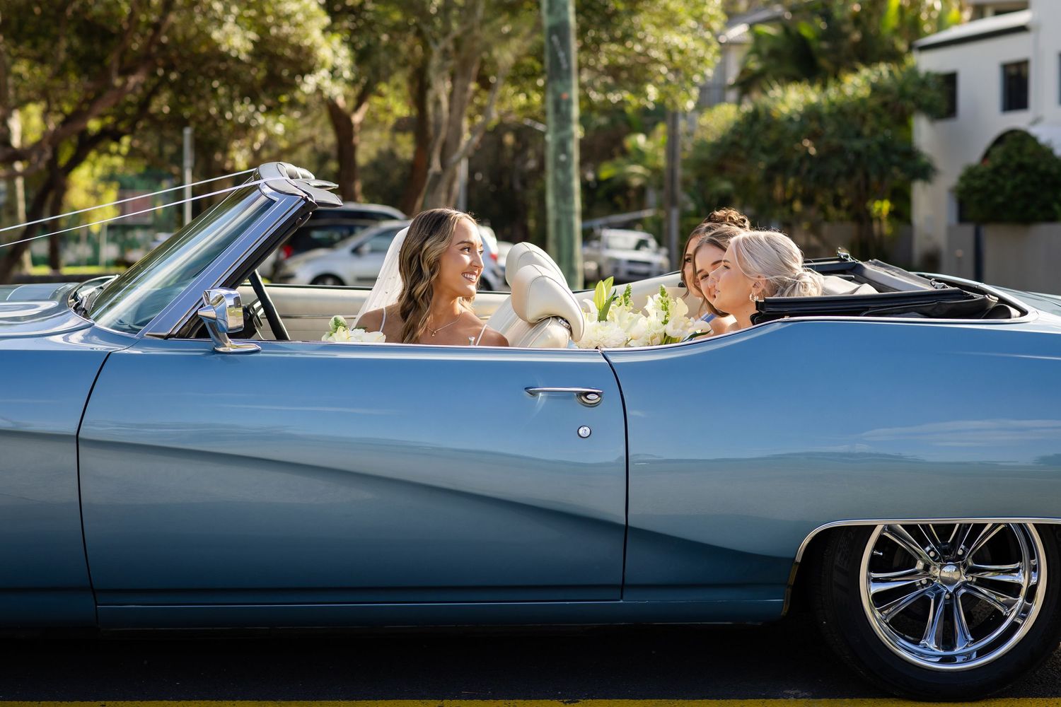 Classic light blue convertible car carries wedding party members along a road.