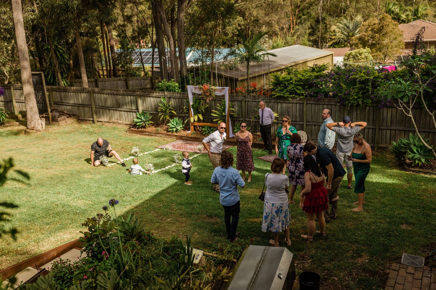 Outdoor wedding reception area with guests gathering in a backyard garden setting.Gold Coast beach wedding photography