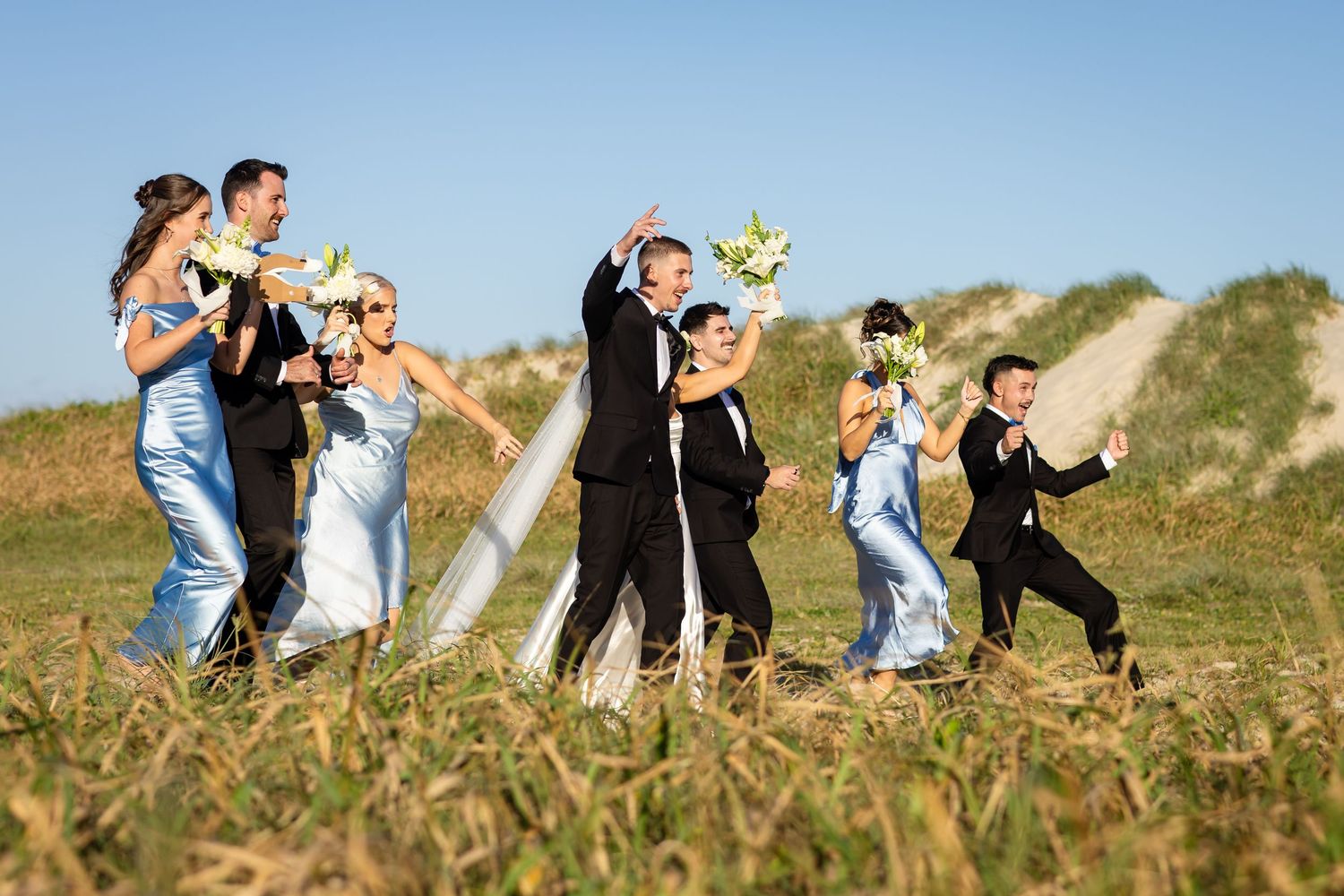 Wedding party walks along a sandy beach path during golden hour.beach wedding currumbin surf club wedding