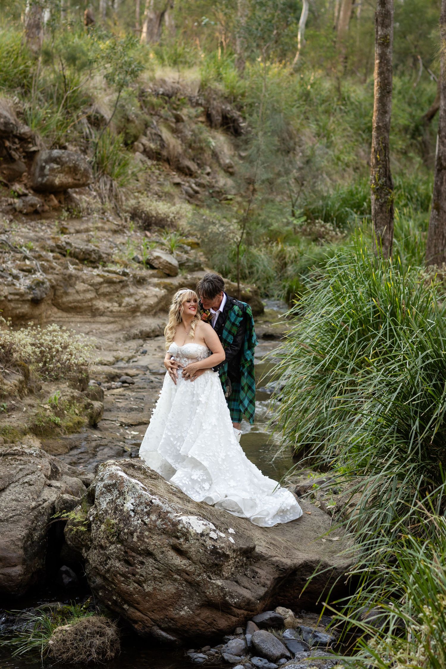 Newlyweds pose on rocky outcrop near stream in Australian bush setting.Gold Coast wedding photographer