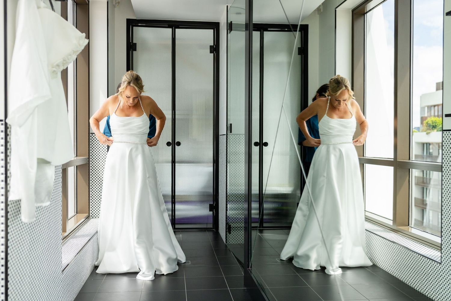 Elegant white wedding dress photographed in a modern hallway with floor-to-ceiling windows.