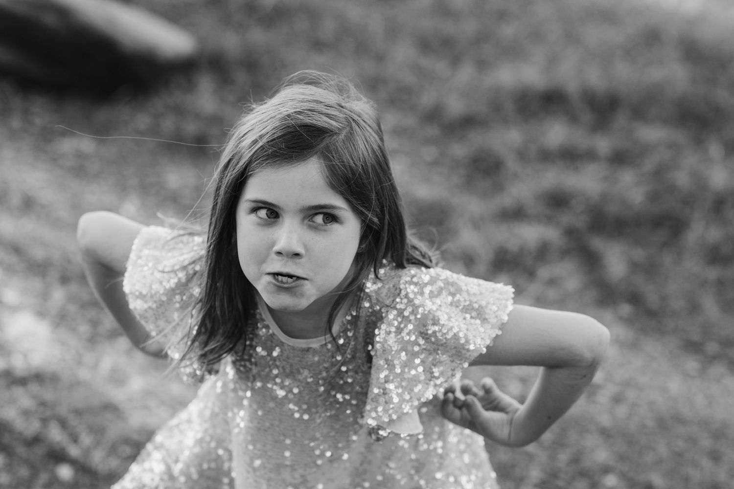 Young person in sparkly dress poses with hands behind head in black and white portrait.Cabarita headland