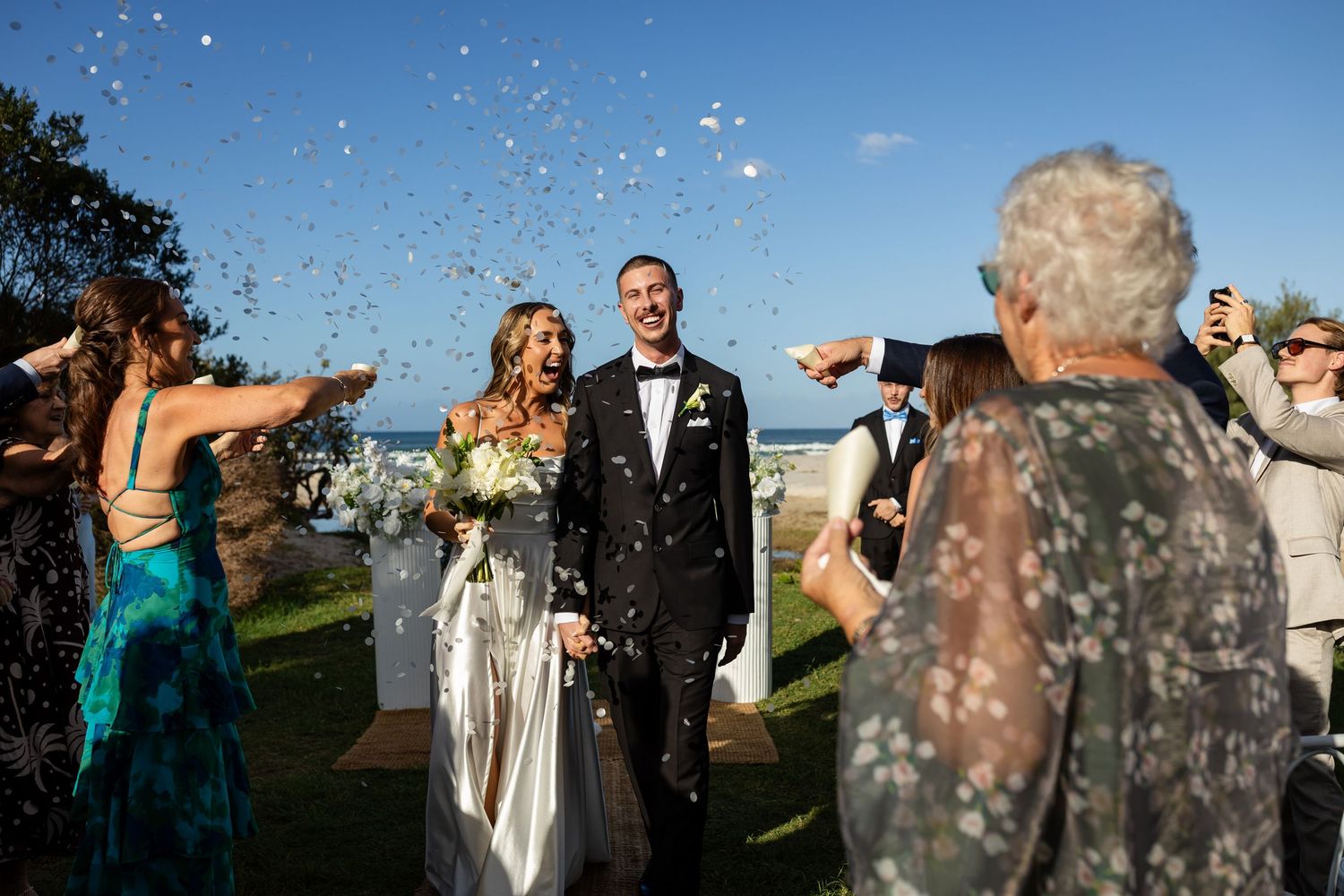 Guests throw confetti during an outdoor beach wedding celebration.beach wedding currumbin surf club wedding