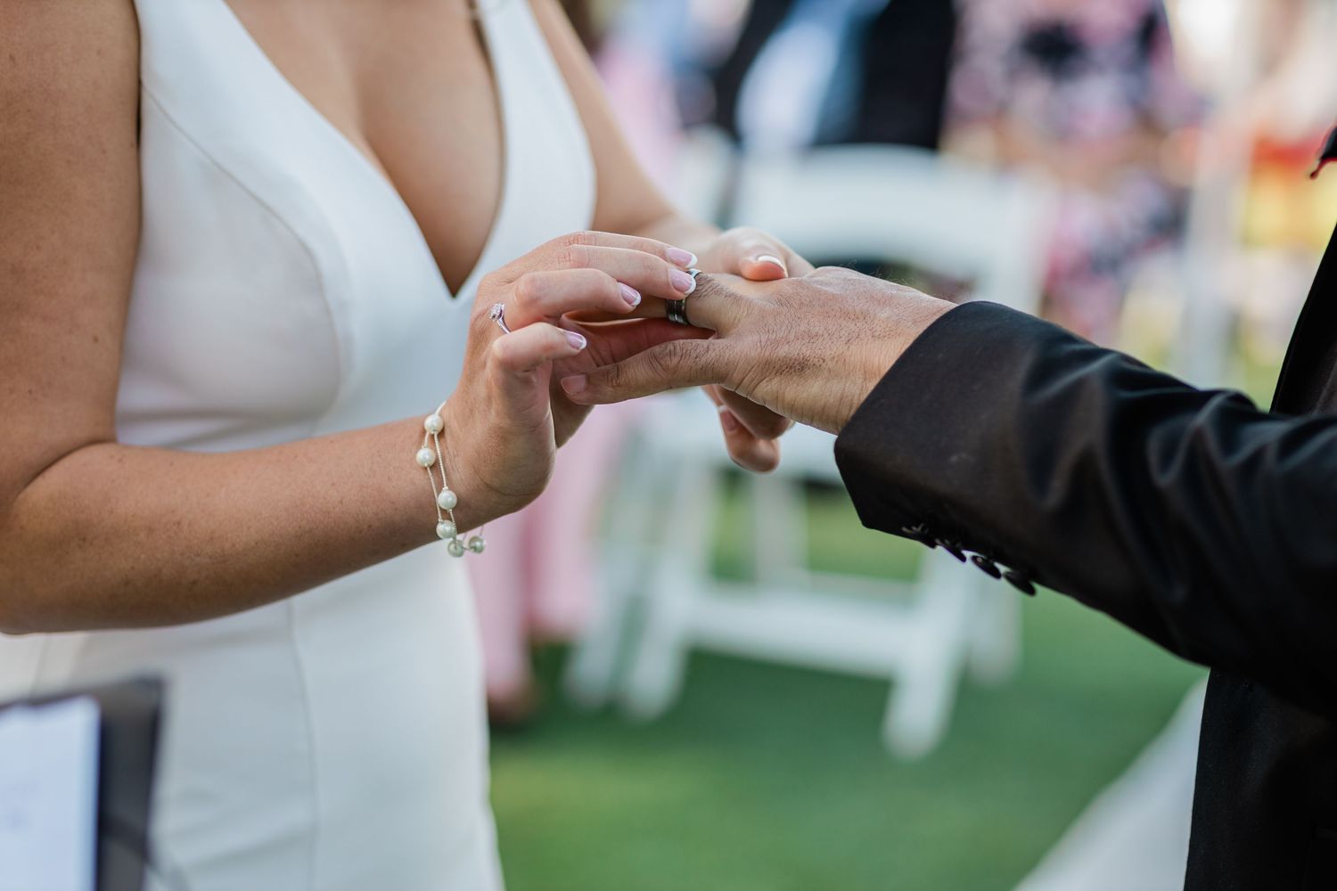 A close-up shot captures the exchange of rings during an outdoor wedding ceremony.