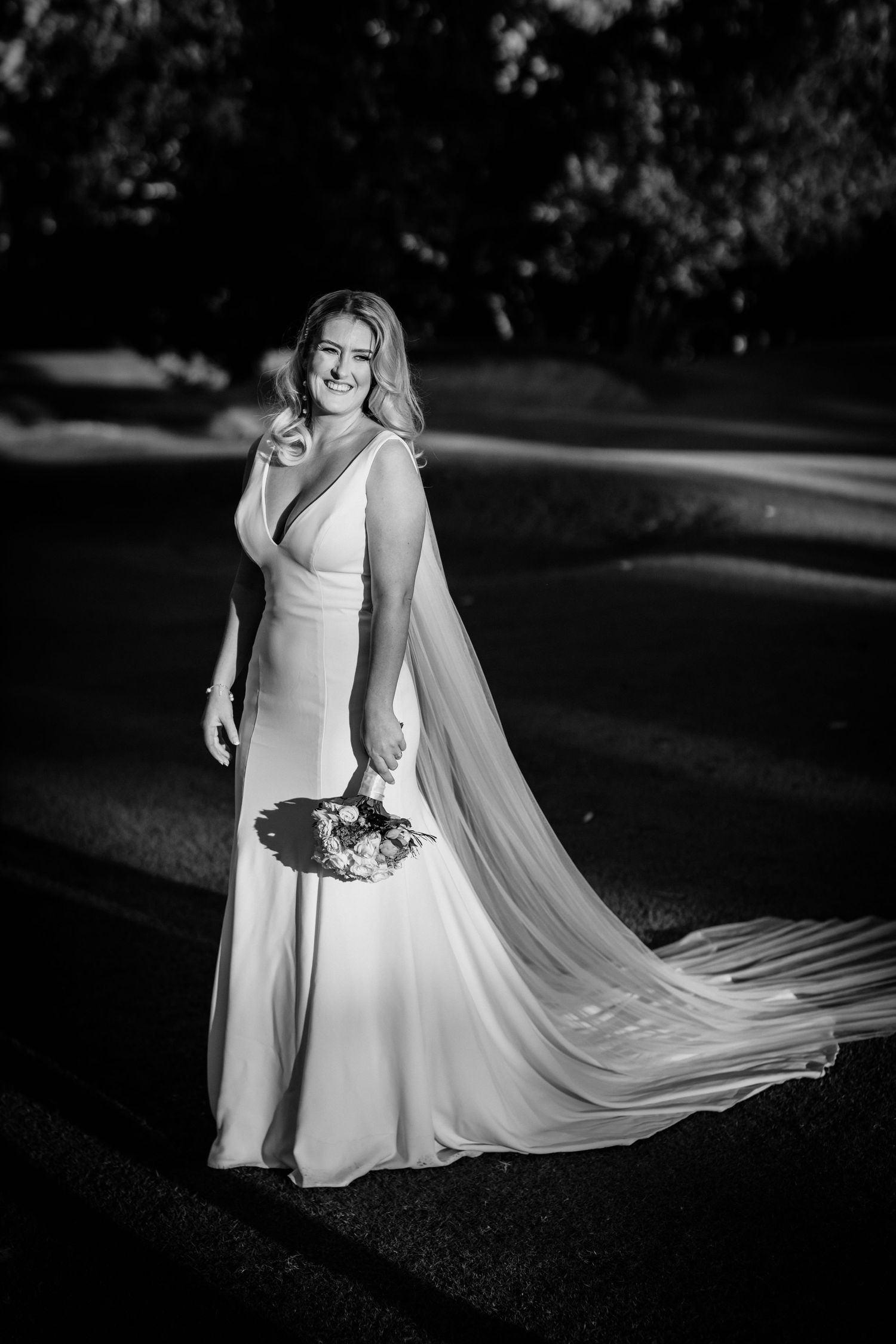 Elegant bride in flowing white dress and veil poses in dramatic black and white portrait.