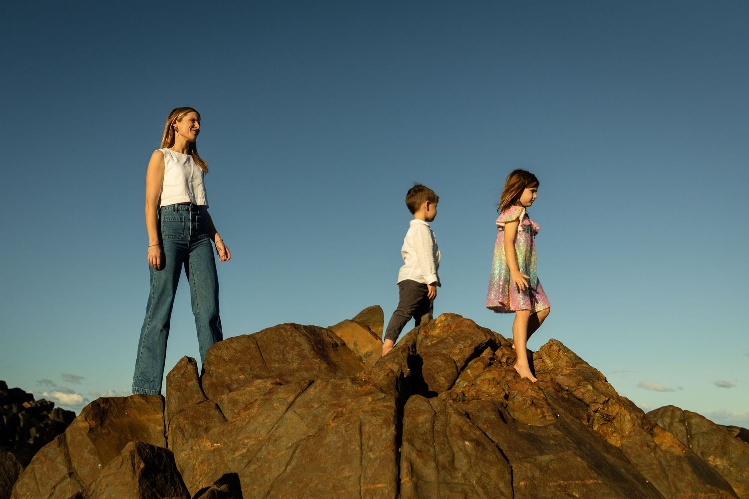 Silhouettes of people standing on rocky outcrop against blue sky.Gold Coast candid family photographer.