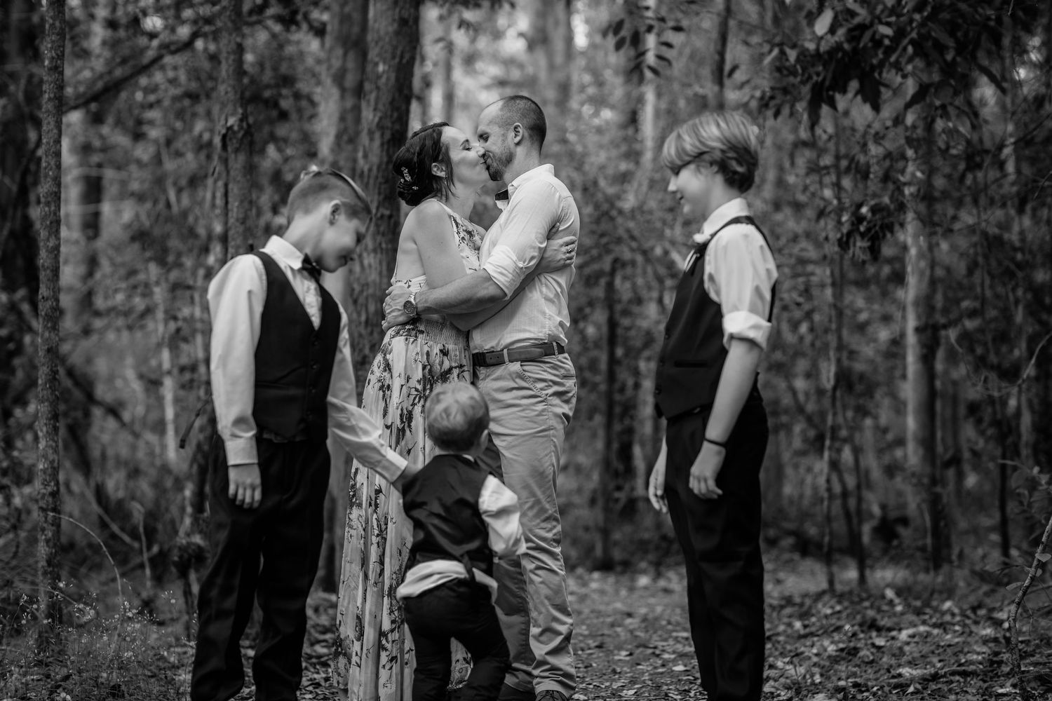 A couple shares an intimate moment among trees in a black and white forest photograph.Gold Coast elopement photographer