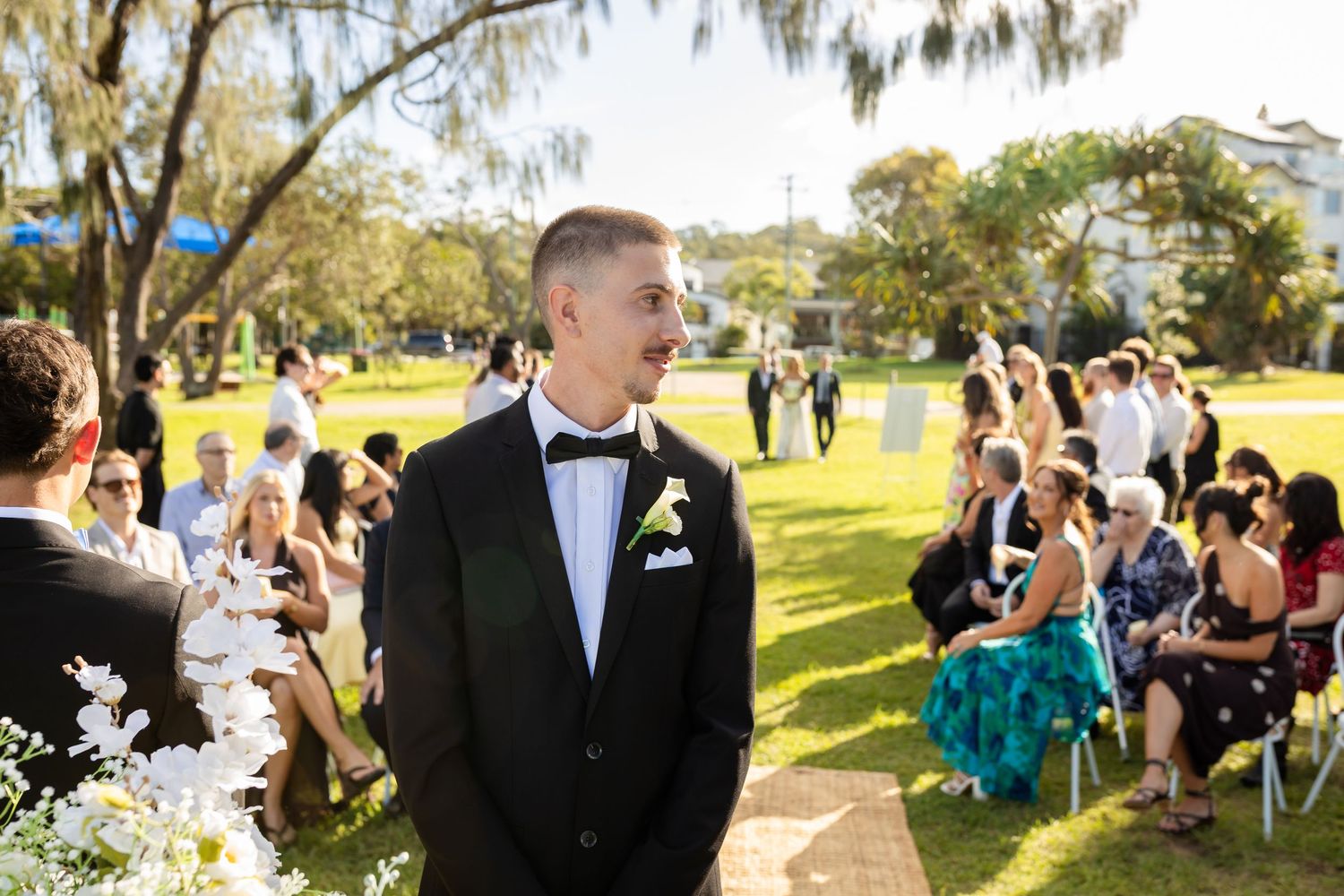 Wedding guests and party members gather for outdoor celebration under trees.