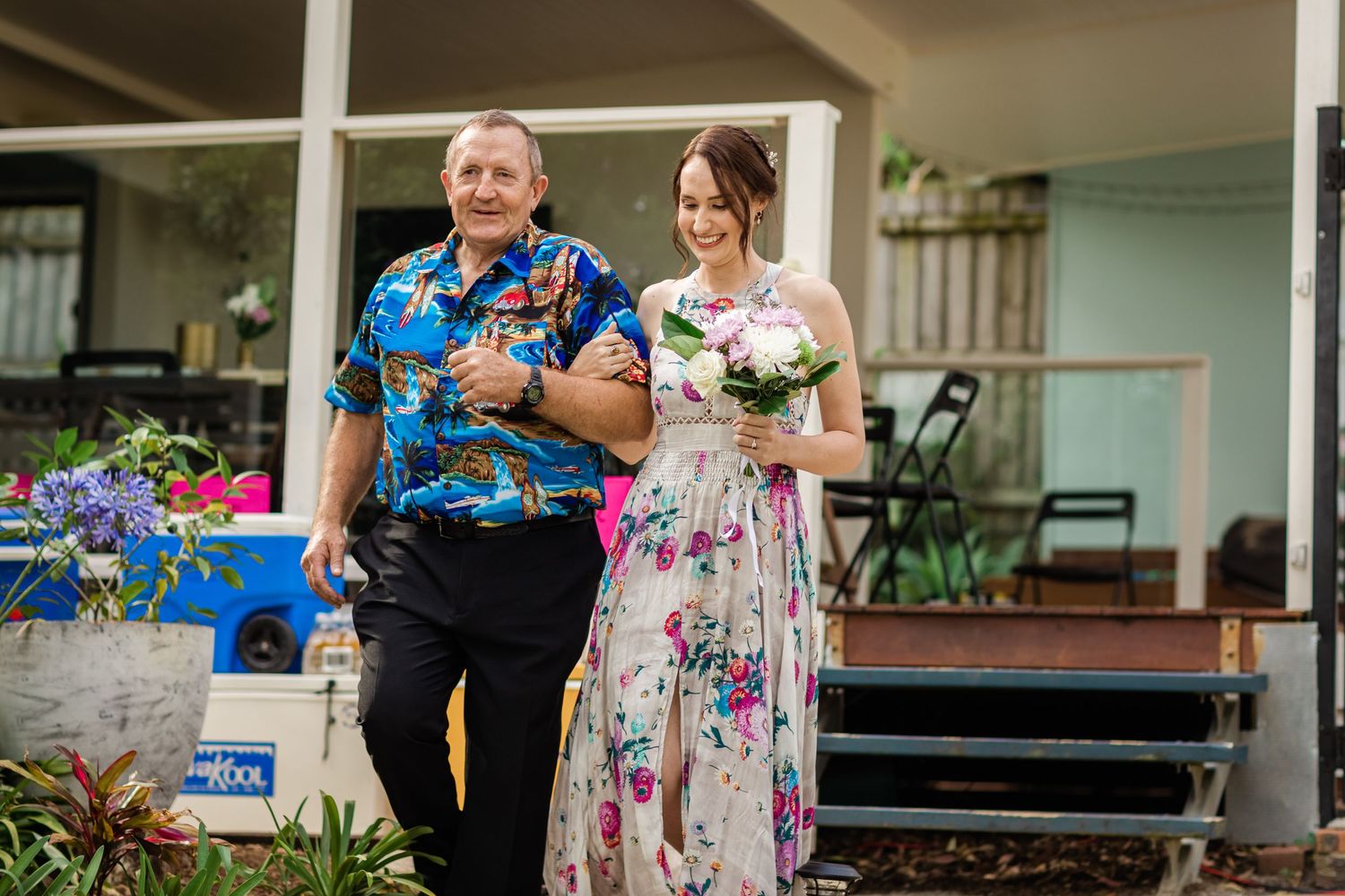 Wedding guests gather outdoors on a sunny day for a casual celebration in a garden setting.