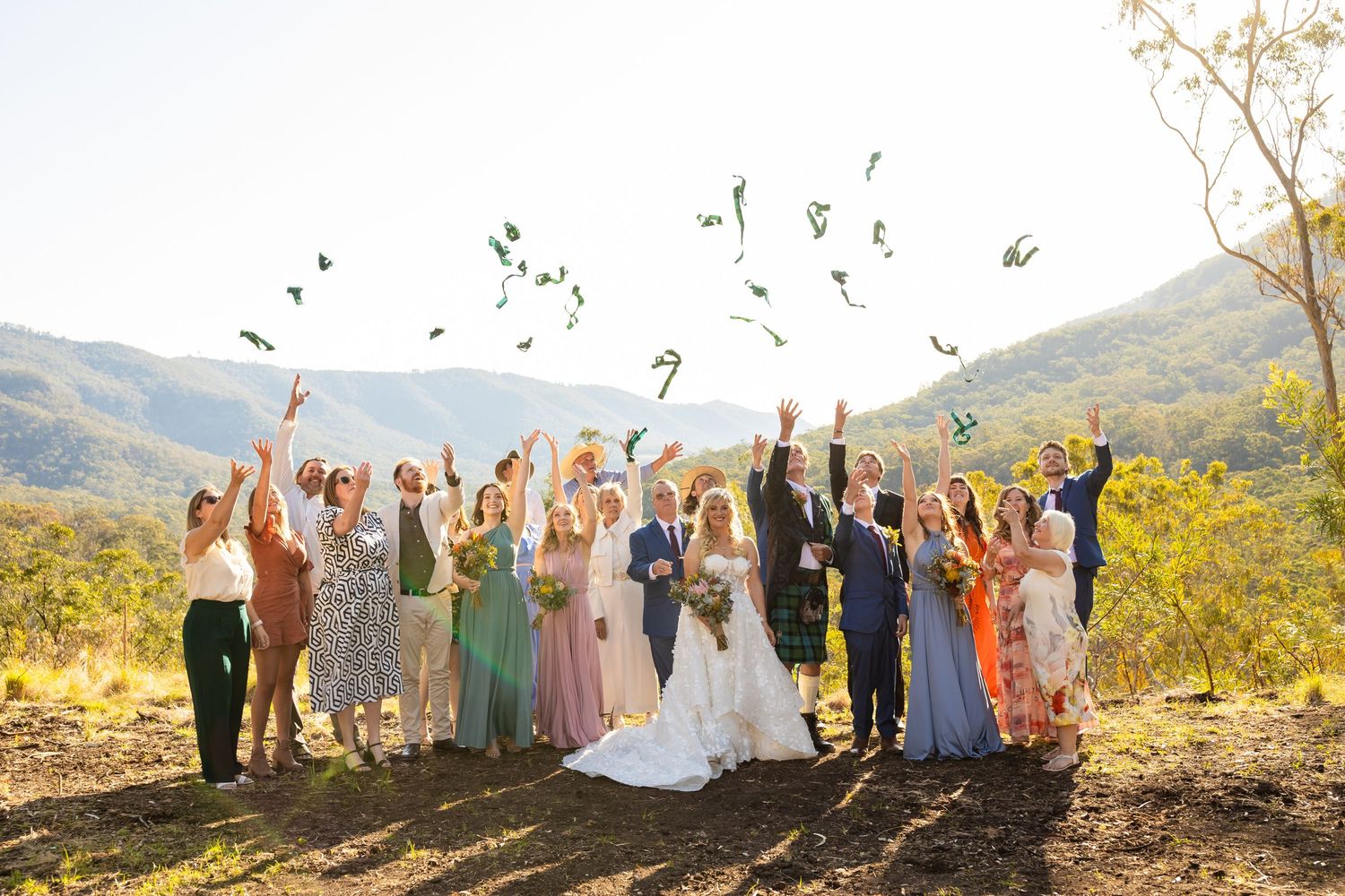 Wedding party and guests celebrate with arms raised against mountain backdrop.Gold Coast wedding photographer