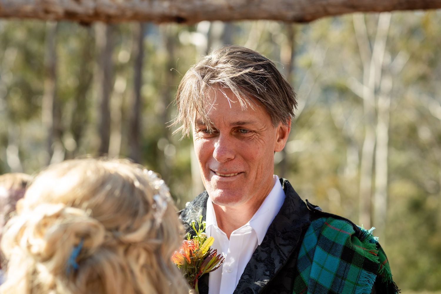 Wedding party members stand together outdoors with autumn foliage in the background.