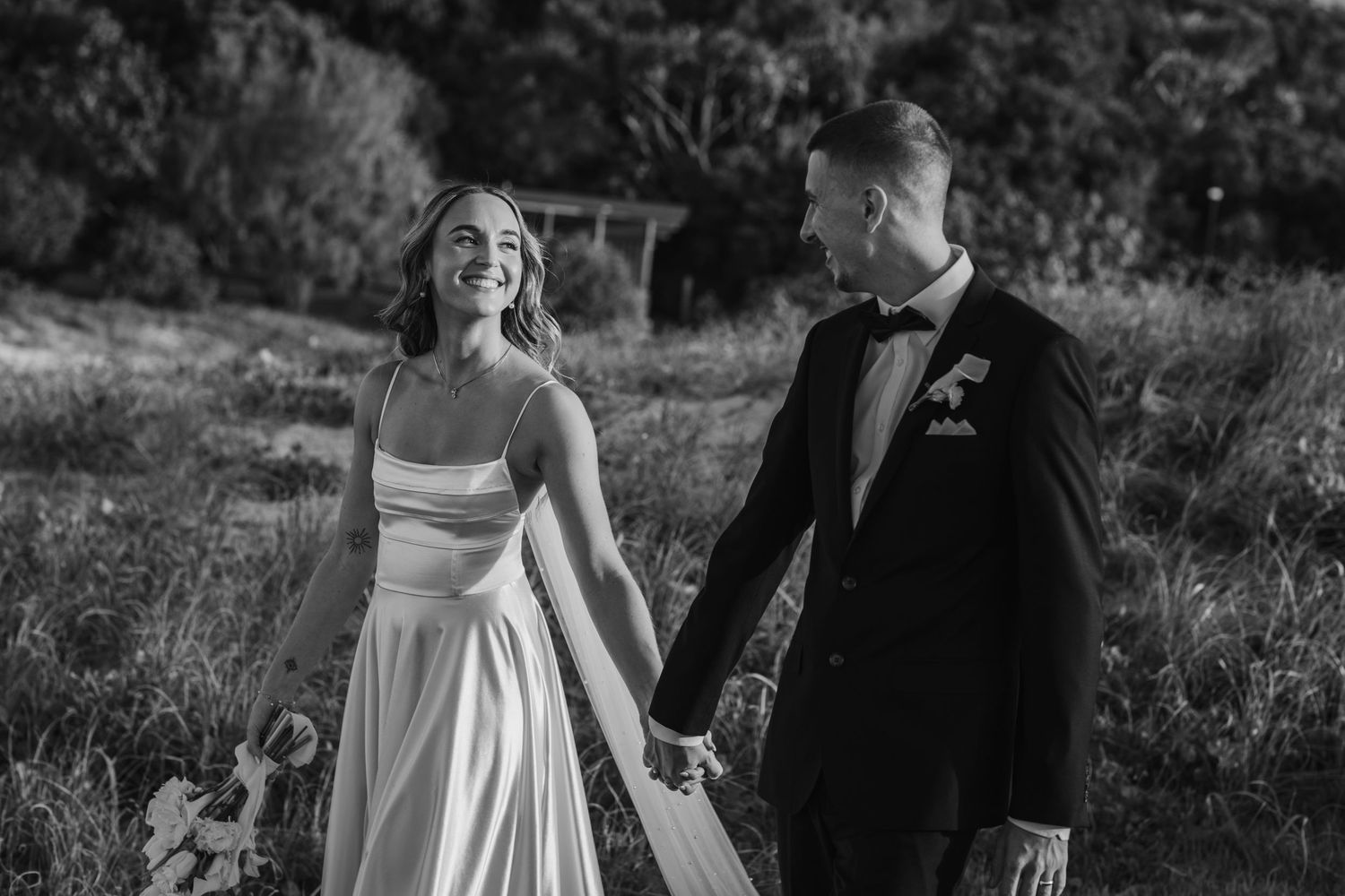 Couple in wedding attire share a joyful moment outdoors in black and white photography.beach wedding currumbin surf club wedding