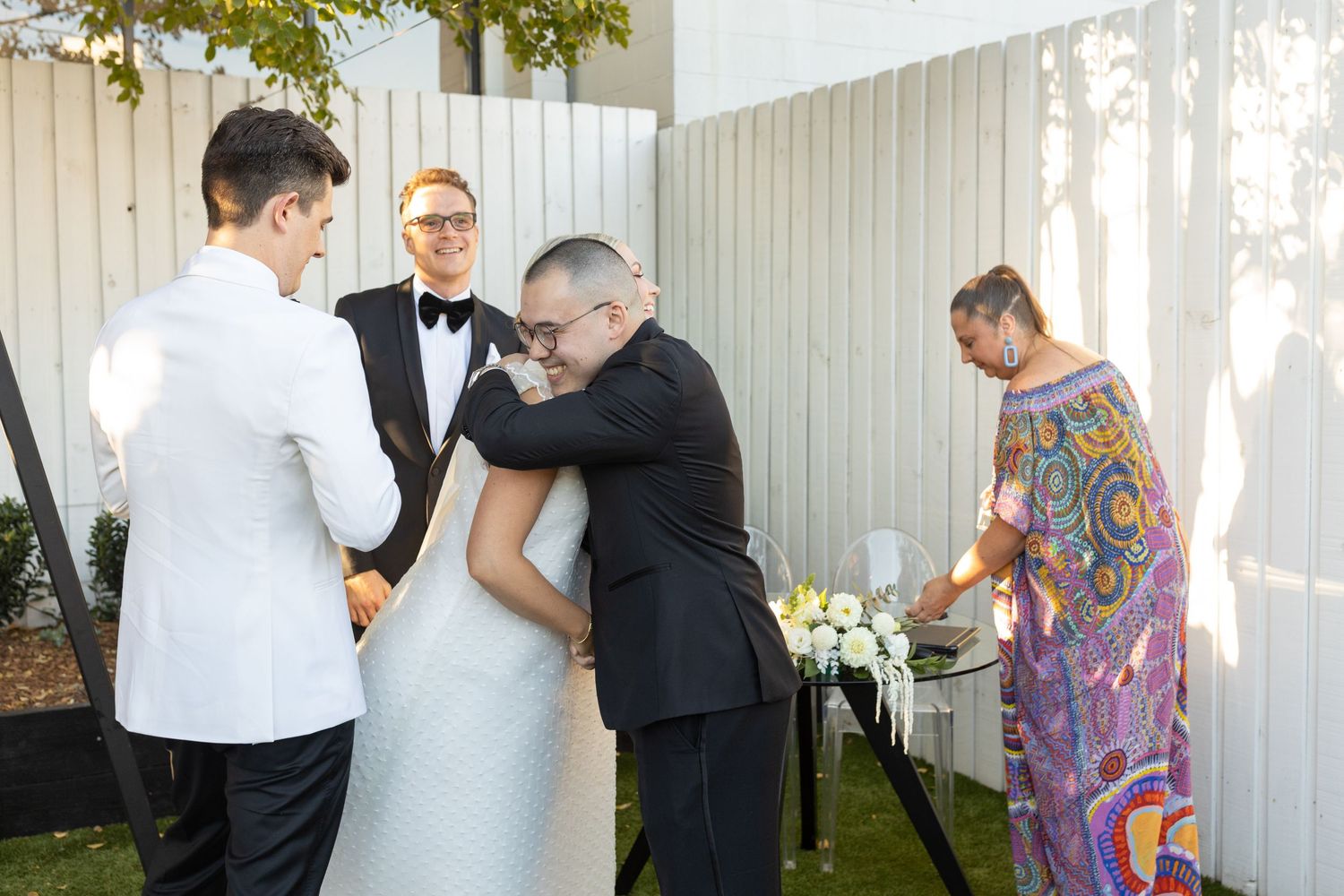 Outdoor wedding reception with guests mingling near white fence.