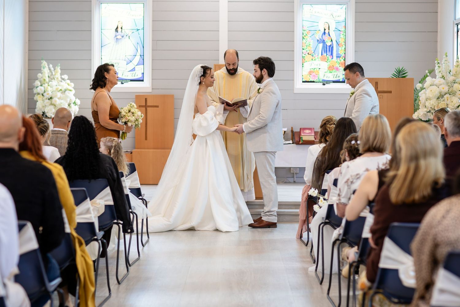 Wedding ceremony in progress inside a modern chapel with gray paneled walls.