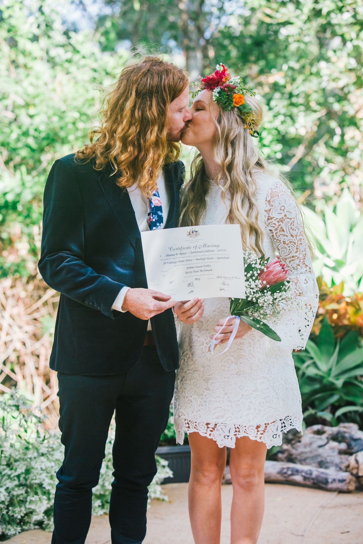 Intimate wedding moment with couple sharing a kiss while holding their marriage certificate.
