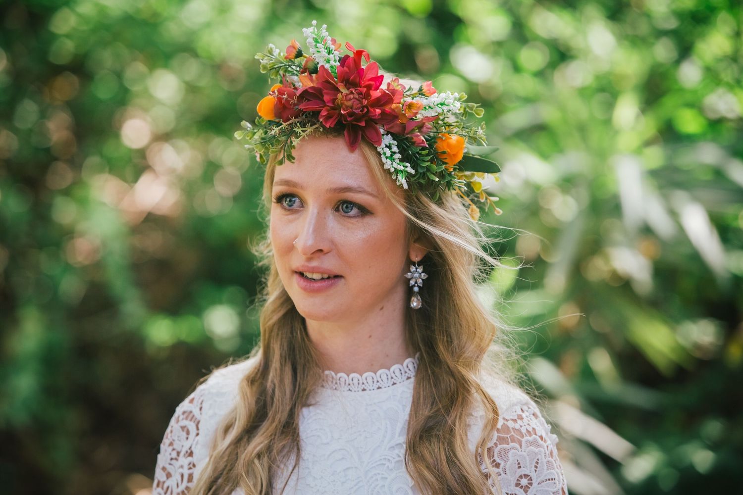 Bride wearing floral crown and lace dress in sunlit garden setting.