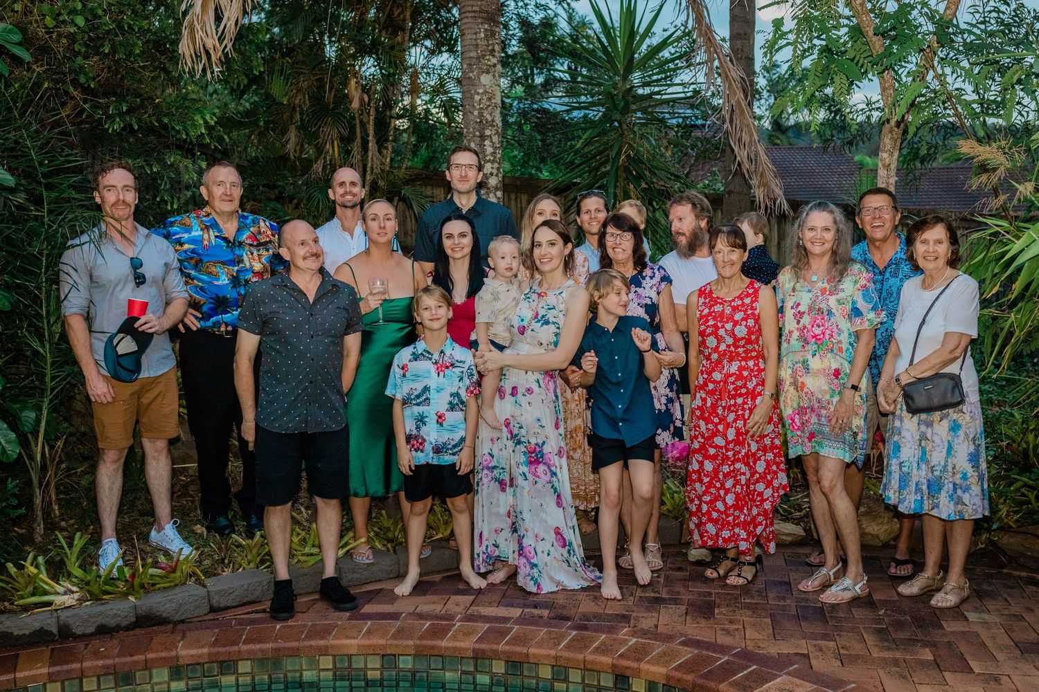 Large group photo of party guests gathered in a tropical garden setting.