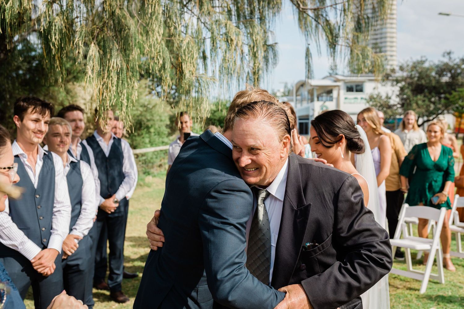 Wedding guests gather under a willow tree for an outdoor ceremony.