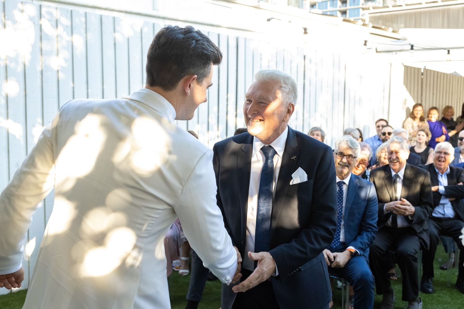 Wedding celebration in sunny outdoor garden with white fence backdrop.