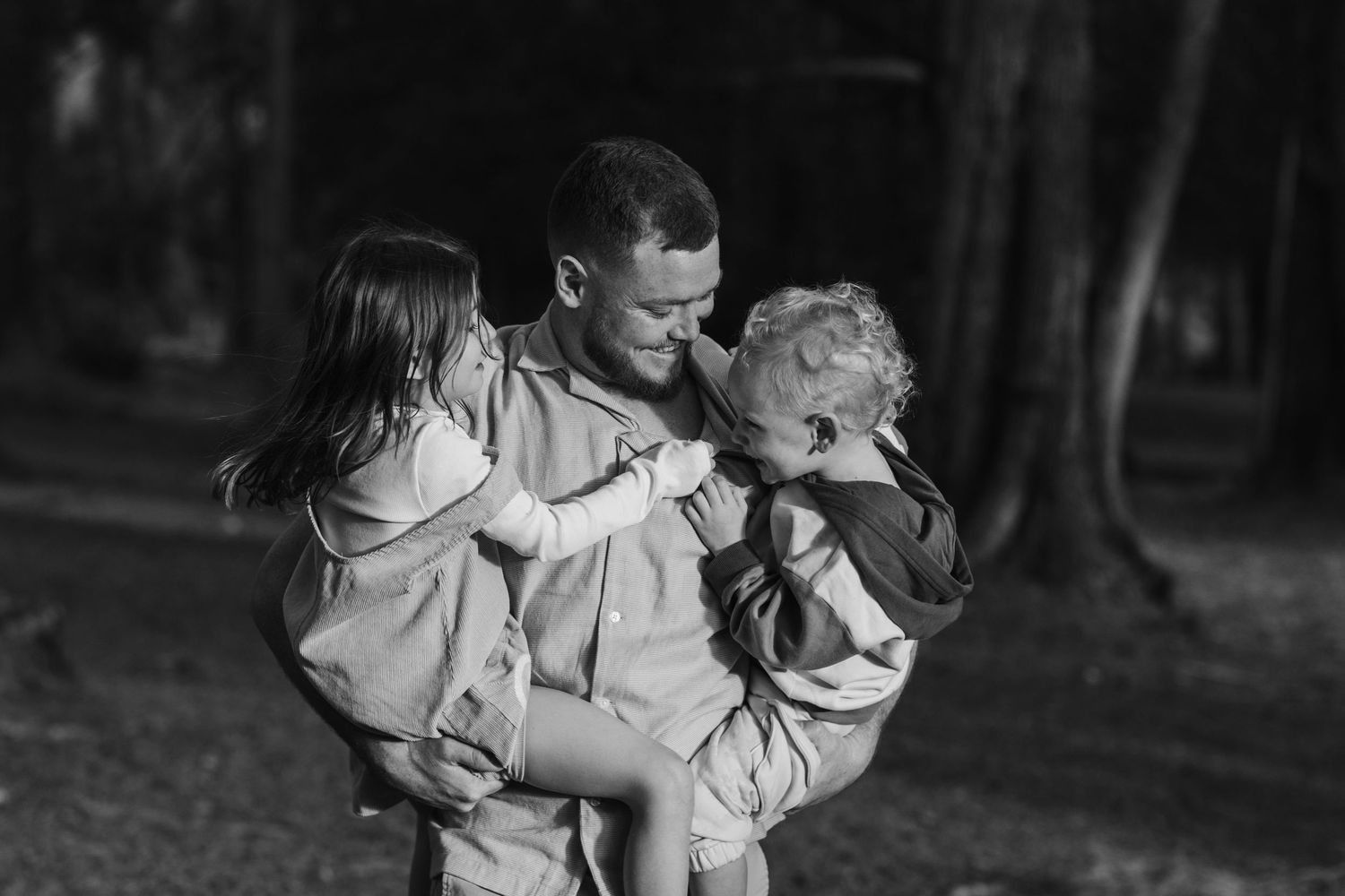 Black and white portrait of loving family embraces in a wooded setting.Tallebudgera family photography. Gold Coast