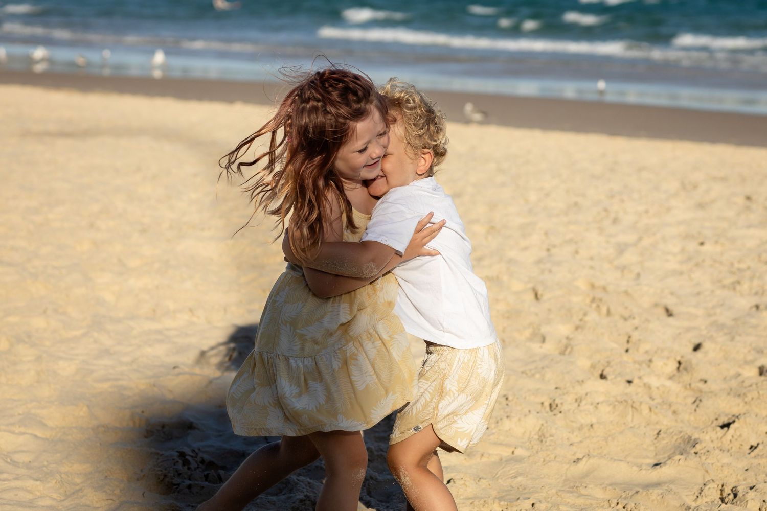 People enjoying a playful moment together on a sunny beach with ocean waves.Gold Coast candid family photographer.