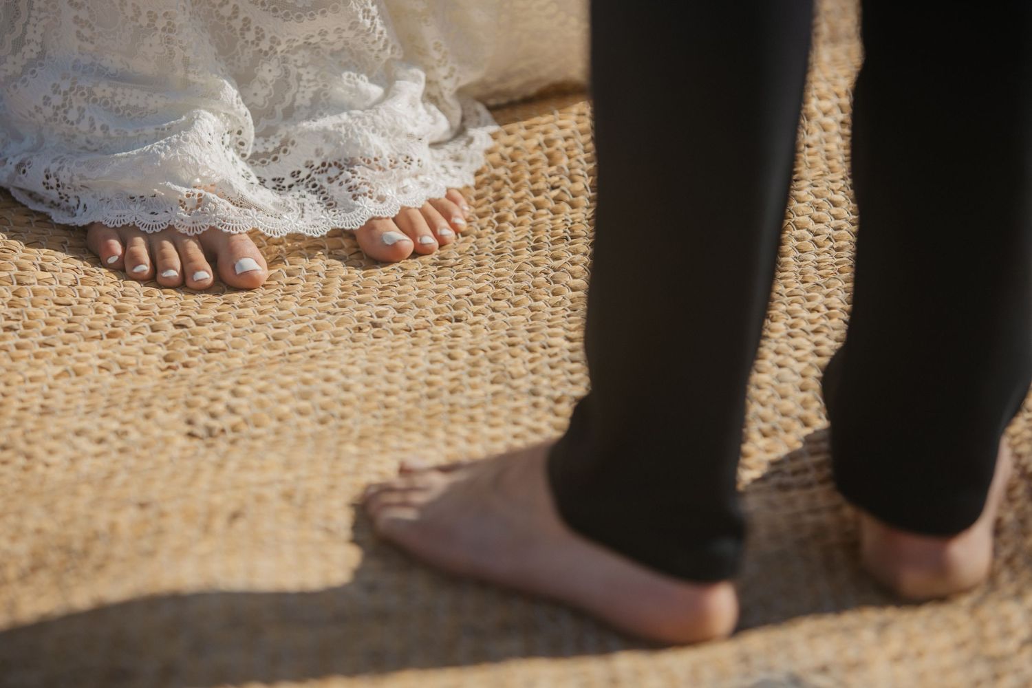 Close-up view of bare feet and formal attire on sandy beach surface.