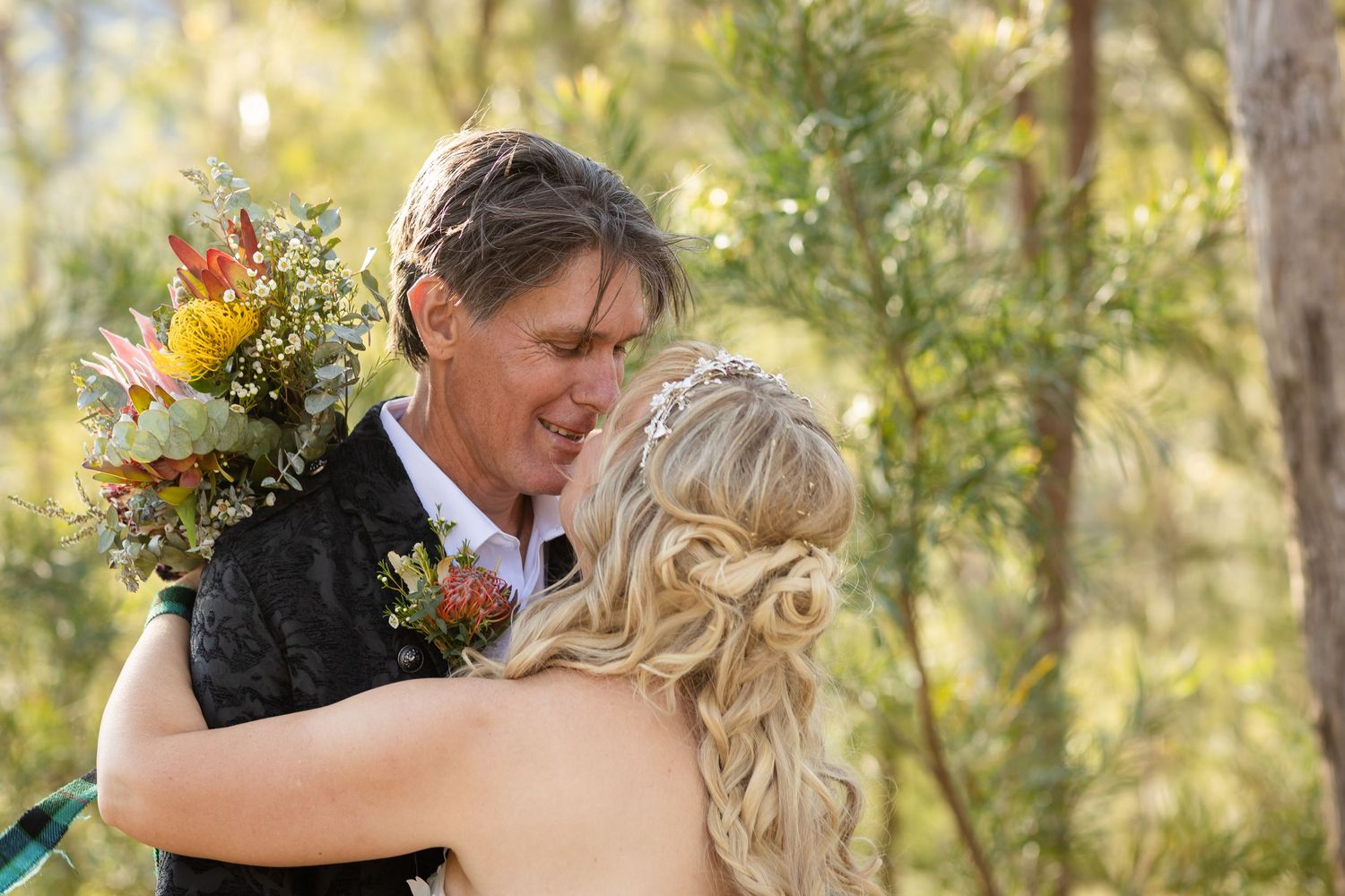 Romantic outdoor wedding moment with couple embracing among sunlit trees and vibrant flowers.Gold Coast wedding photographer
