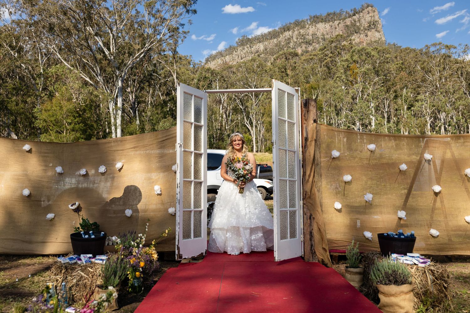 Elegant outdoor wedding setup with white doors and red carpet against mountain backdrop.
