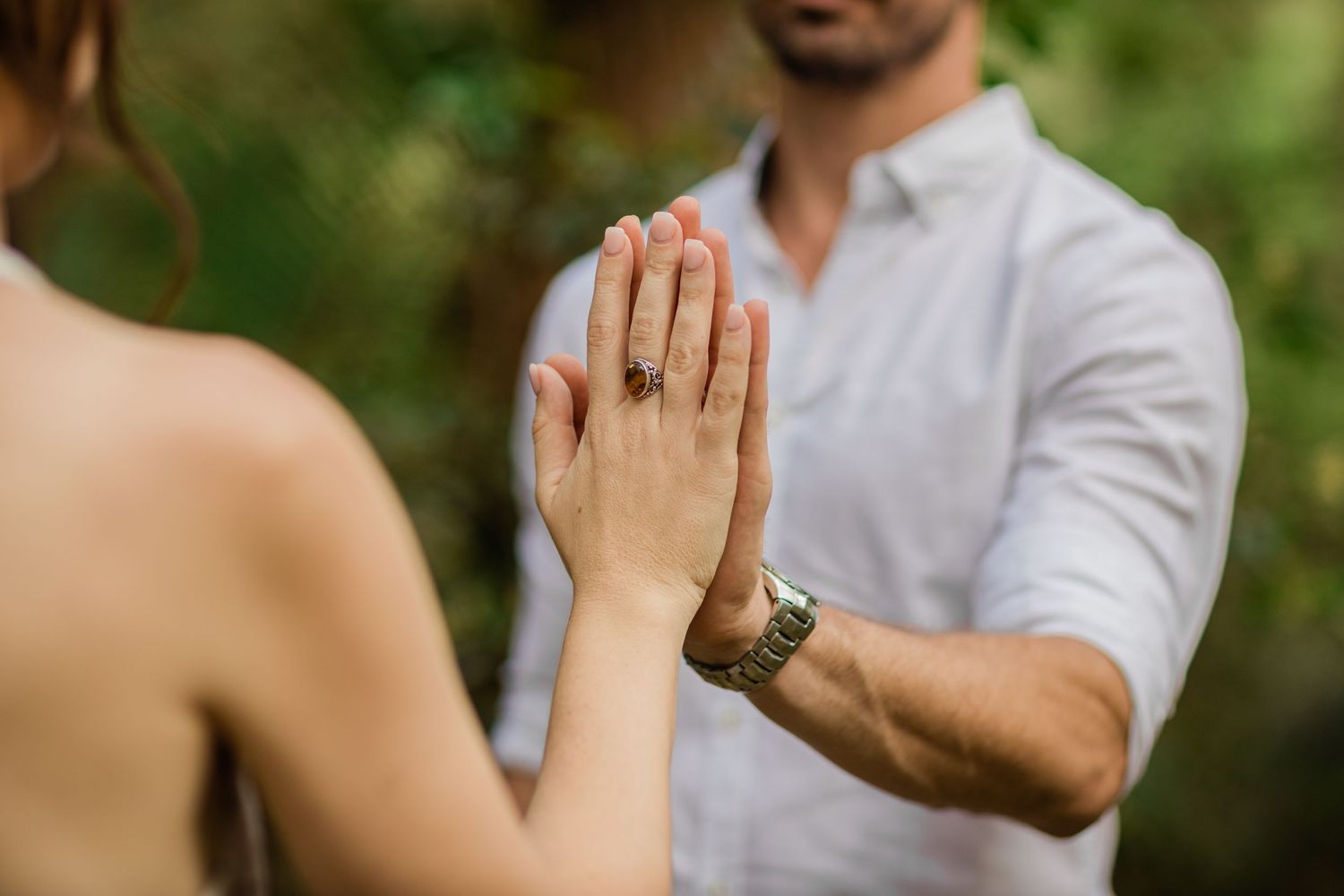 Close-up shot of hands touching in an intimate moment against a blurred forest background.Gold Coast elopement photographer