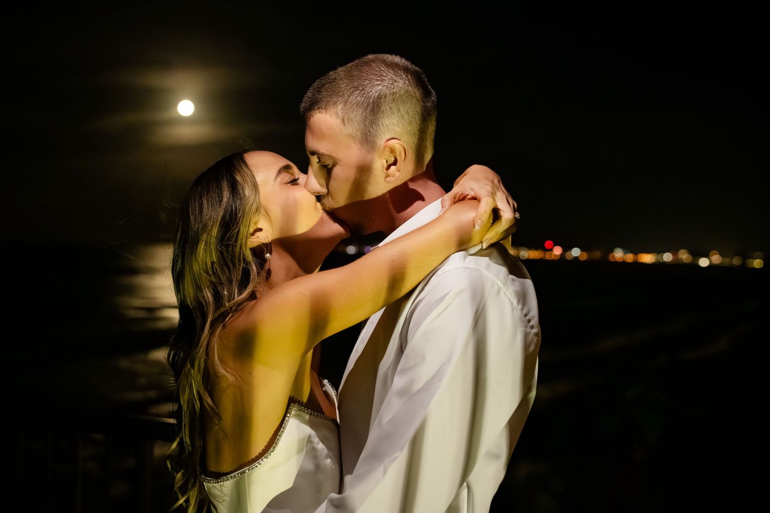 Romantic moonlit moment between newlyweds with city lights in the background.beach wedding currumbin surf club wedding