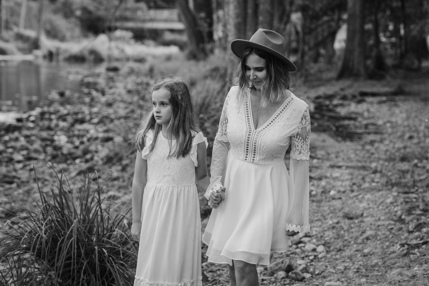 Two figures in white dresses and hats stand together on a forest path in black and white.Tallebudgera family photography. Gold Coast family