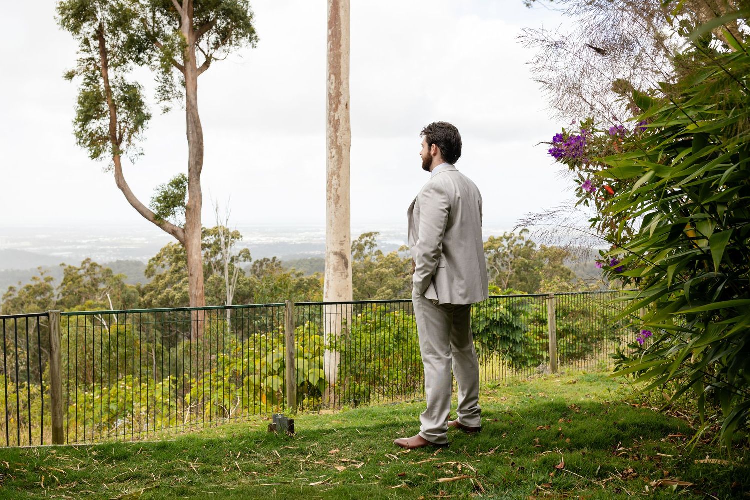 A person in grey suit stands at scenic overlook with mountain views and trees.Gold Coast hinterland wedding photographer