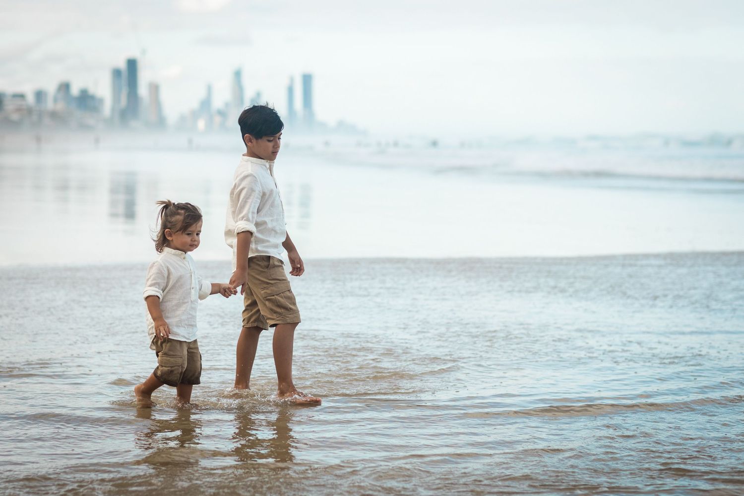 Family enjoying a sunset walk along a misty beach with city skyline in the background.Gold Coast candid family photographer.