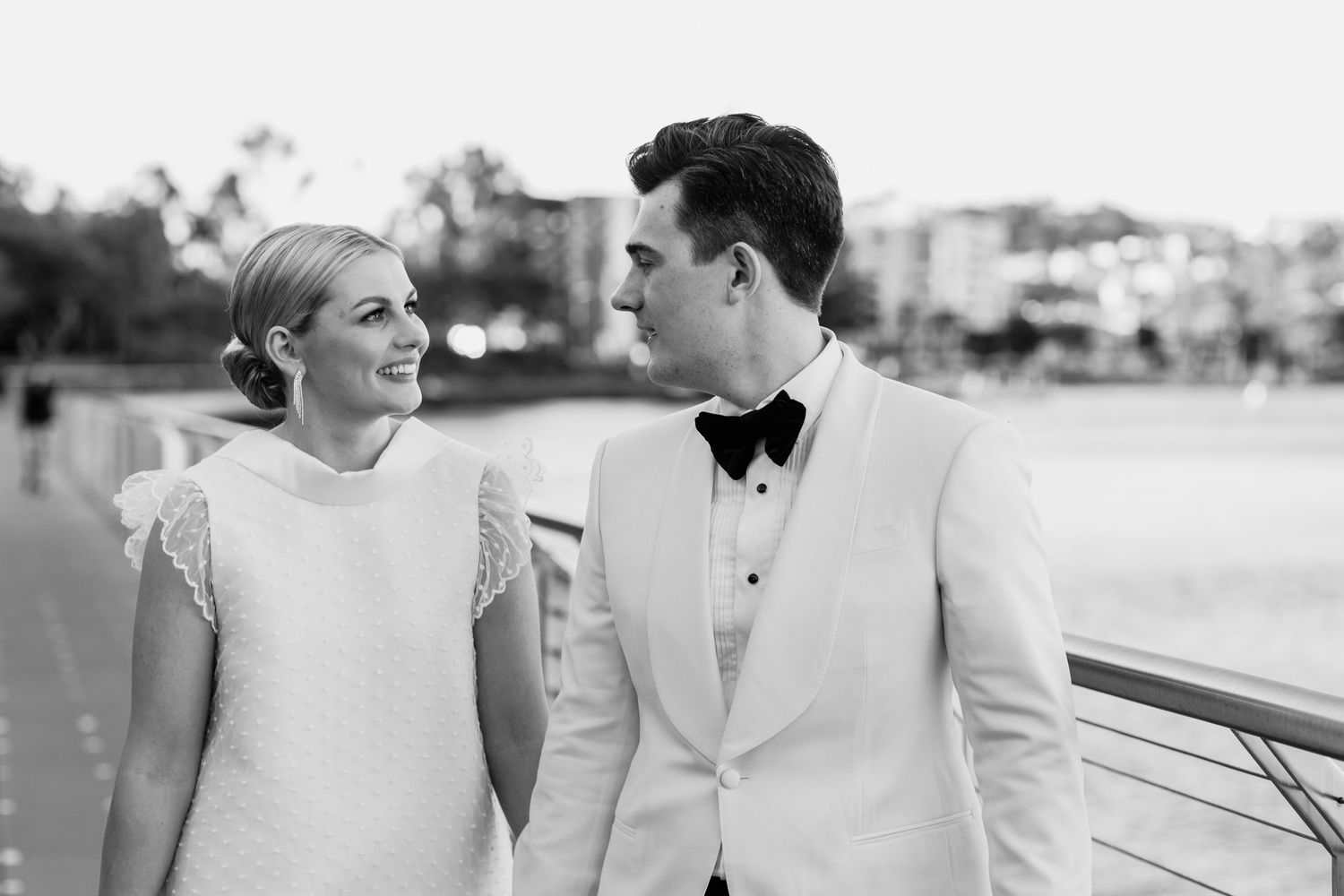 Elegant bride and groom in white attire pose together by the waterfront.