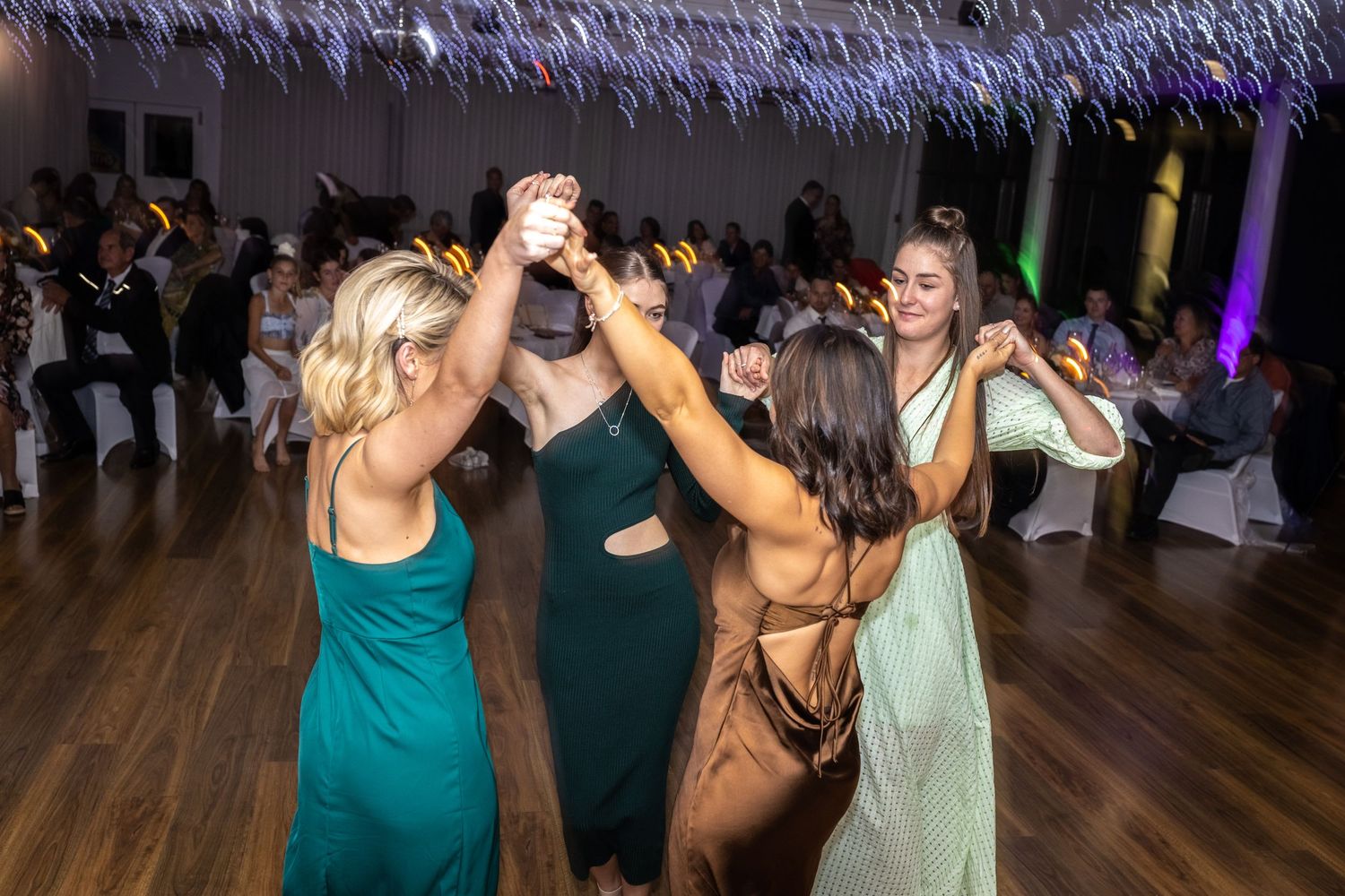 Group dancing energetically at wedding reception with colorful lighting.