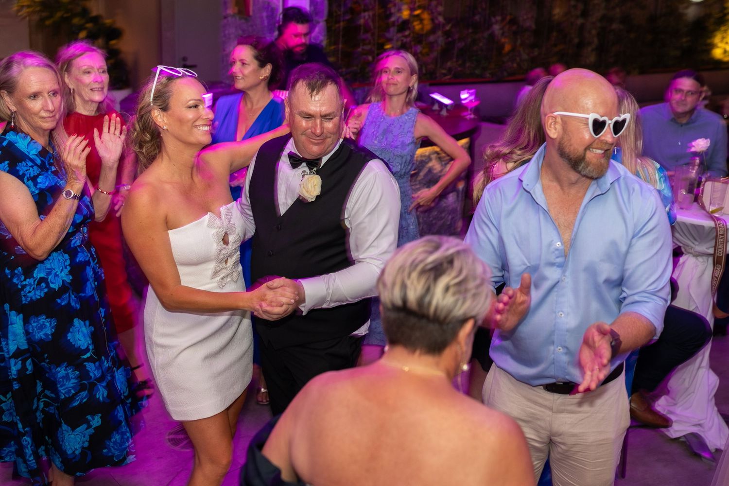 Energetic dance floor moments captured during wedding reception with purple ambient lighting.