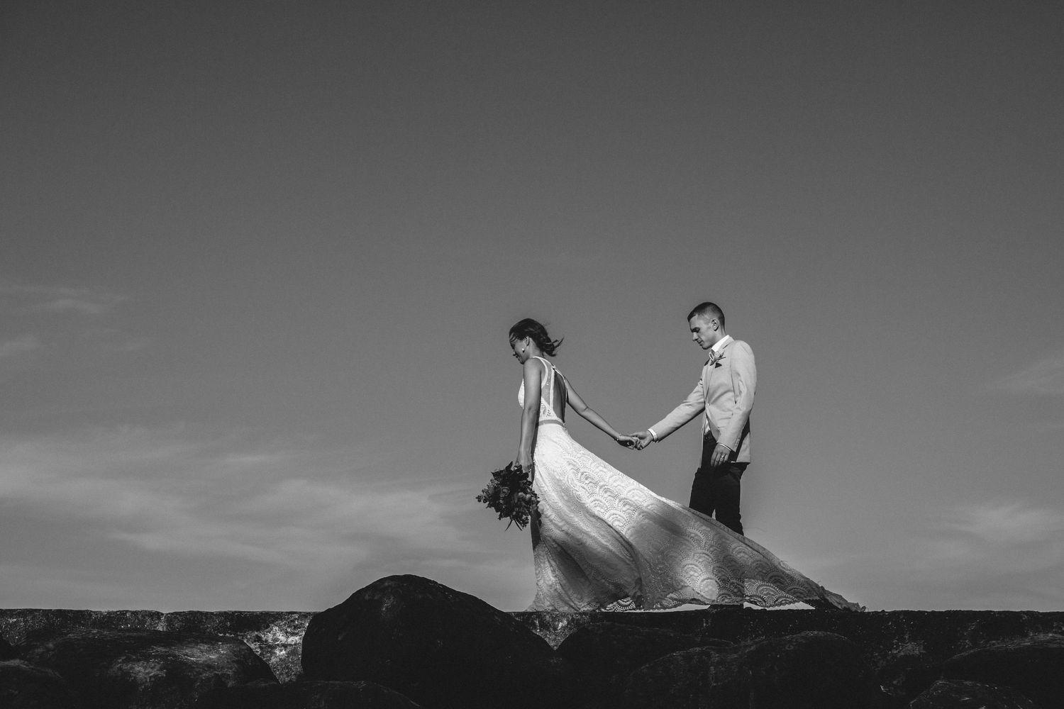 Black and white portrait of couple with flowing wedding dress on rocky terrain.Gold Coast beach wedding photography. Froggies beach
