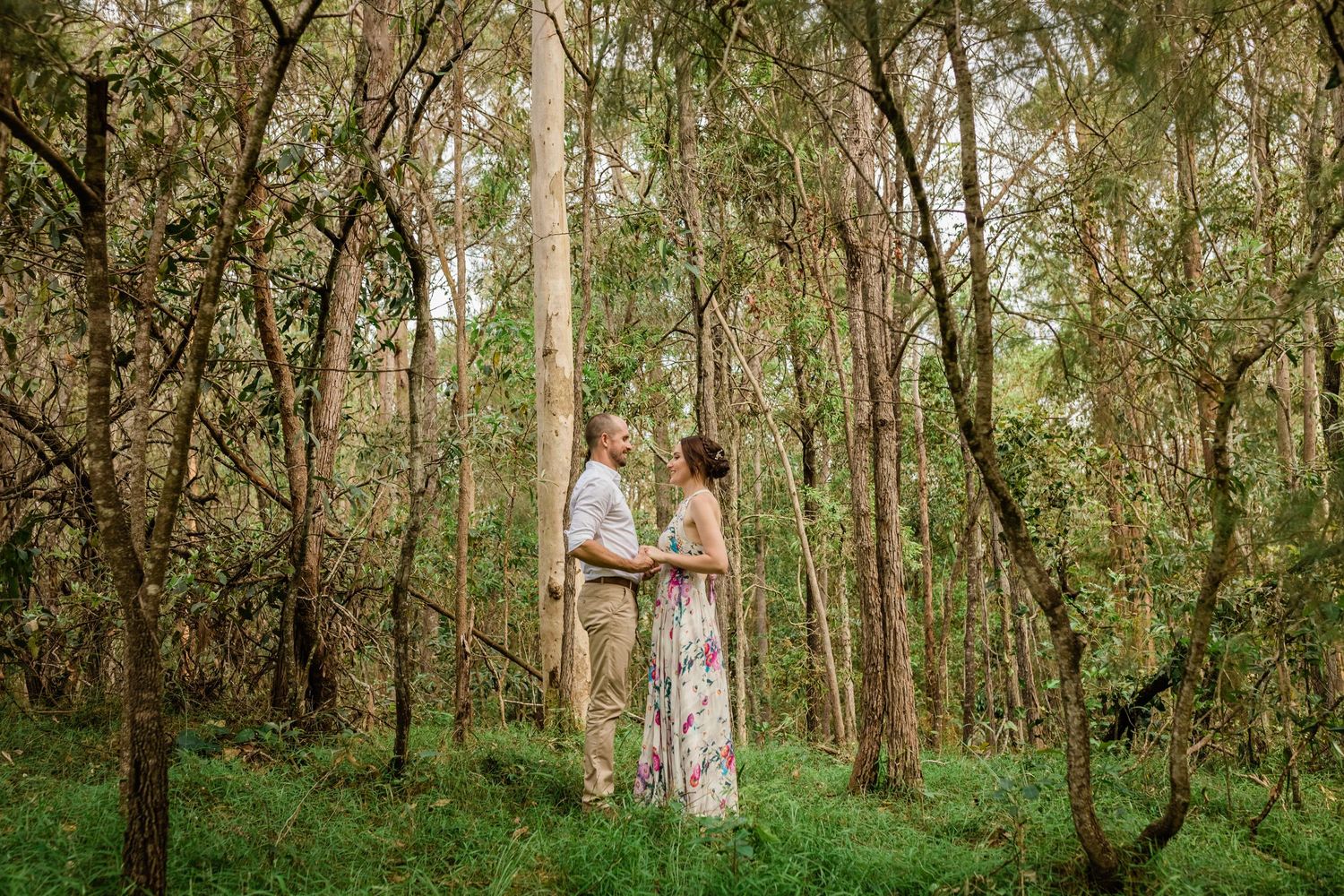 A romantic couple stands together in a sunlit wooded area with tall trees creating a natural backdrop.Gold Coast elopement photographer