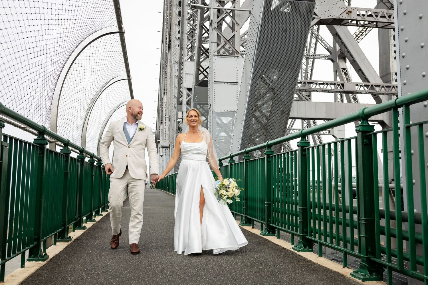Wedding group walks down green metal staircase with urban backdrop.