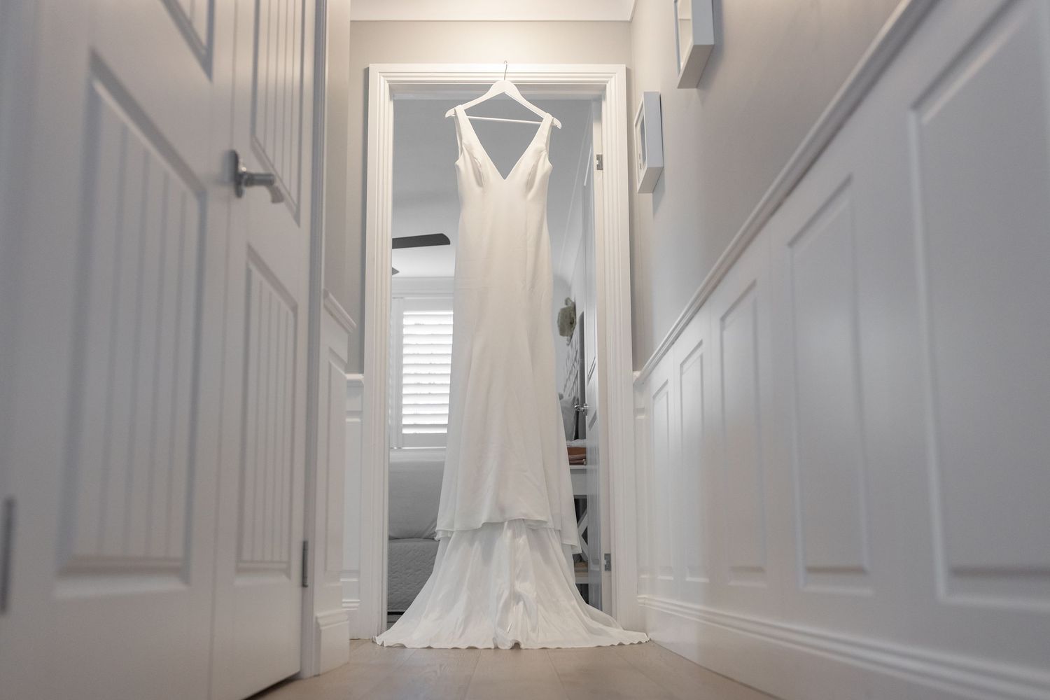 A white wedding dress hangs elegantly in a bright hallway with white walls and doors. Surfers Paradise Golf Club wedding.