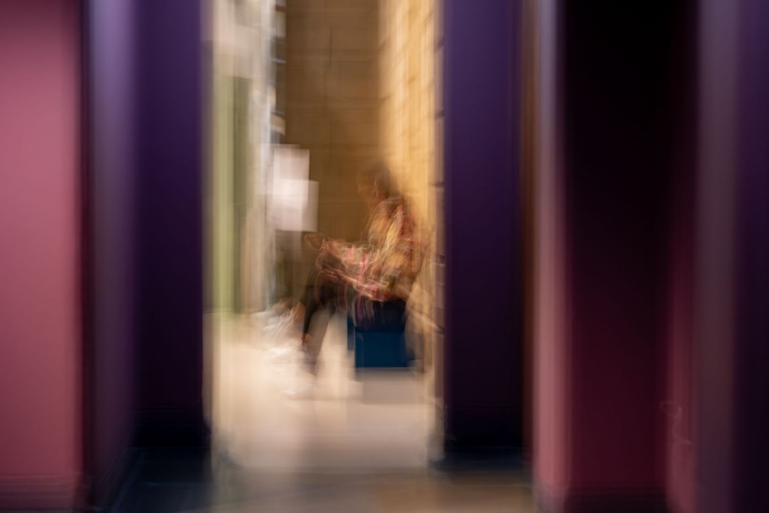 Blurred artistic photograph showing a figure through a doorway with purple and pink tones.