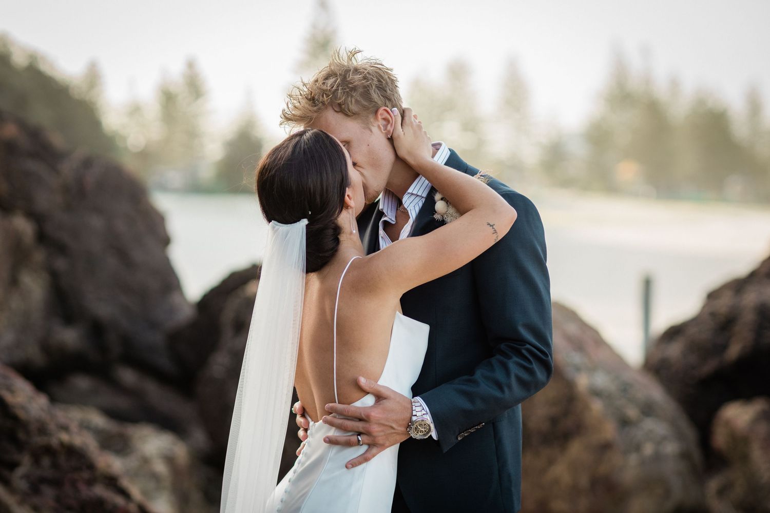 Wedding couple sharing intimate moments among pine trees in outdoor setting.