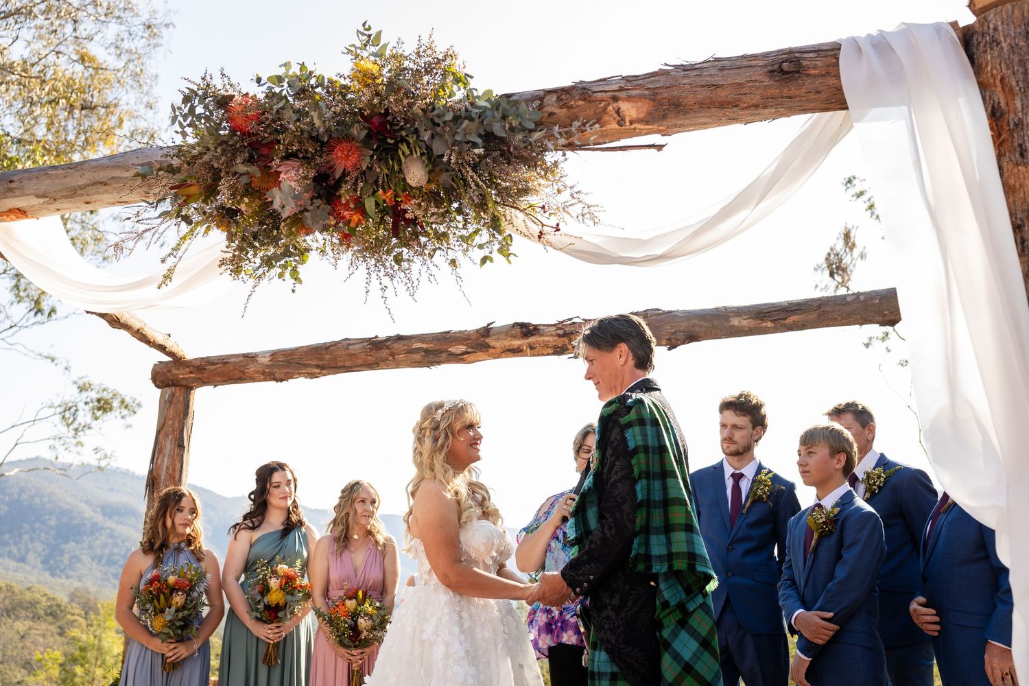 Wedding ceremony under wooden arch with mountain views and floral decorations.Gold Coast wedding photographer