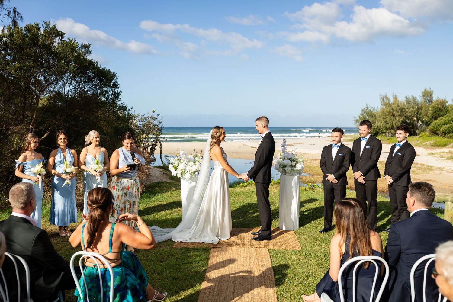 Wedding ceremony setup on a grassy lawn with white chairs and ocean views.